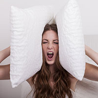 Äußere Einflüsse Frau schreit und hebt sich zwei Kissen auf die Ohren