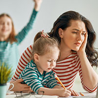 Psychische Einflüsse Junge Mutter sitzt vor dem Laptop mit Kind auf dem Schoß und 2. Kind im Hintergrund