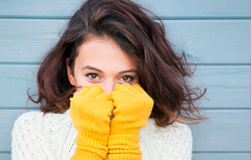Frau hält gelbe Handschuhe ins Gesicht und lächelt