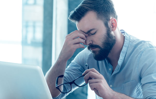 Mann sitzt vor dem Laptop und fasst sich an die Stirn