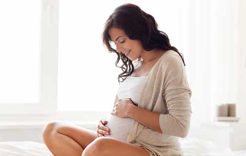 Schwangere Frau sitzt auf dem Bett und berührt ihren Bauch