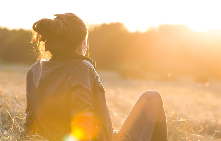 Junge Frau auf Stoppelfeld schaut in die Abendsonne